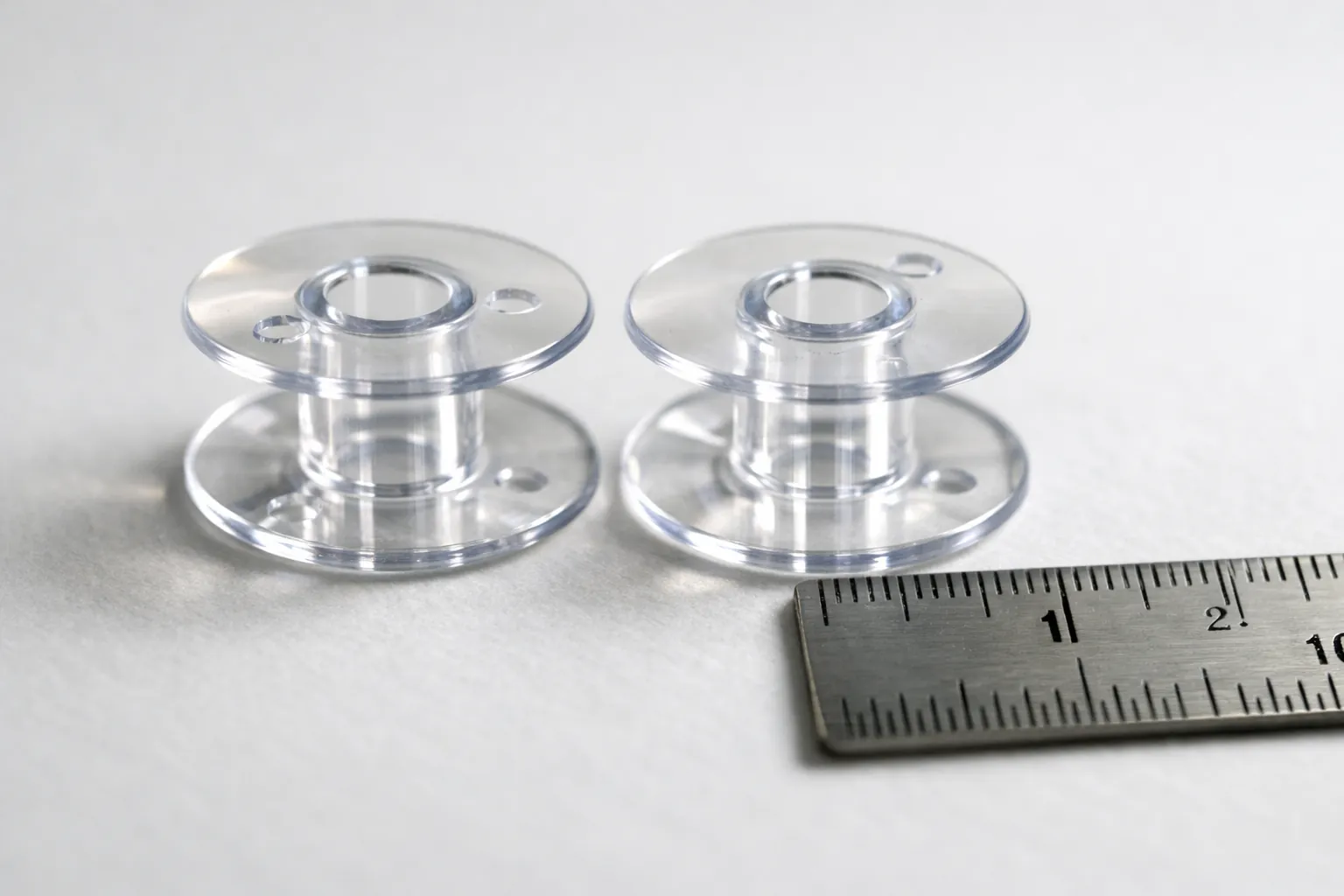 Two similar clear bobbins beside a small steel ruler